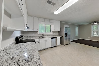 Kitchen featuring appliances with stainless steel finishes, a sink, white cabinetry, a textured ceiling, and plenty of natural light