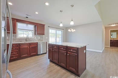 Kitchen featuring reddish brown cabinets, light stone countertops, decorative backsplash, stainless steel appliances, and a kitchen island