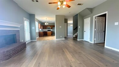 Unfurnished living room with visible vents, baseboards, wood finished floors, stairway, and ceiling fan with notable chandelier