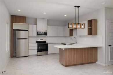 Kitchen featuring light marble finish floors, appliances with stainless steel finishes, a peninsula, backsplash, and recessed lighting