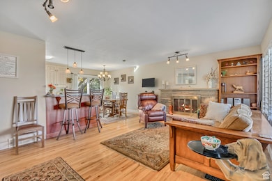 Living area featuring rail lighting, light wood finished floors, a stone fireplace, and a chandelier