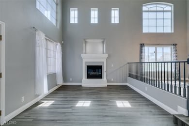 Unfurnished living room featuring a high ceiling, healthy amount of natural light, wood finished floors, and a glass covered fireplace