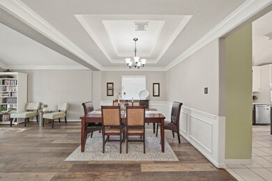 The formal dining room exudes elegance with its decorative wall accents and classic chair rail molding. A stunning tray ceiling with multiple recessed tiers and intricate crown molding adds depth to the space. Overhead, a dark bronze chandelier with five frosted glass shades provides a warm, inviting glow that perfectly completes the room’s upscale ambiance.