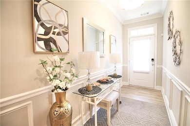 Entrance foyer featuring a decorative wall, crown molding, and a wainscoted wall