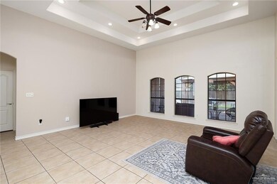 Living room with light tile patterned floors, a towering ceiling, a tray ceiling, and ceiling fan