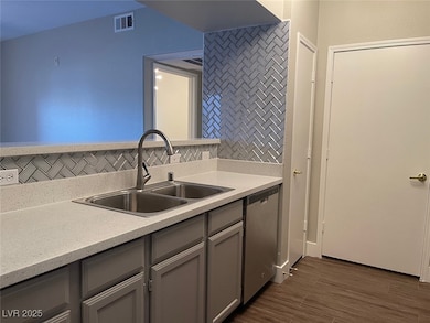 Kitchen featuring tasteful backsplash, gray cabinetry, stainless steel dishwasher, light stone counters, and dark wood-type flooring
