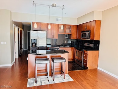 Kitchen featuring glass insert cabinets, stainless steel appliances, decorative light fixtures, tasteful backsplash, and a kitchen breakfast bar