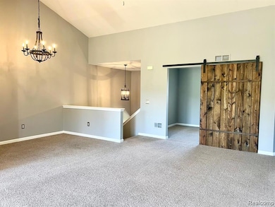 Unfurnished room with a chandelier, carpet floors, a barn door, and vaulted ceiling