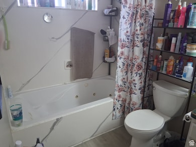 Bathroom with a combined bath / shower with jetted tub, toilet, and wood finished floors