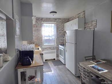Kitchen featuring brick wall, white cabinets, white appliances, radiator, and light countertops