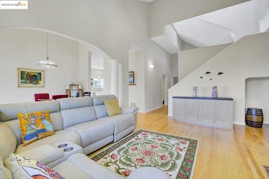 Living room featuring light wood finished floors, a high ceiling, arched walkways, and ornate columns