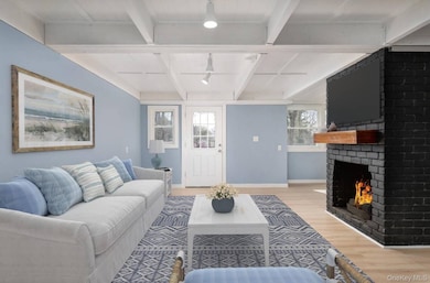 Living room featuring beamed ceiling, wood finished floors, healthy amount of natural light, and a brick fireplace