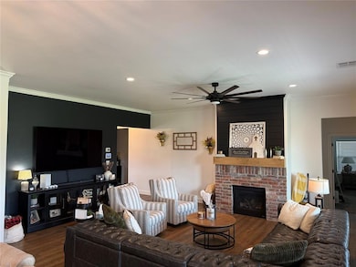 Living area featuring wood finished floors, a ceiling fan, a brick fireplace, ornamental molding, and recessed lighting