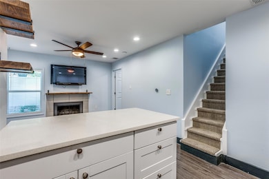 Kitchen featuring white cabinets, dark wood-style flooring, a fireplace, light stone countertops, and recessed lighting