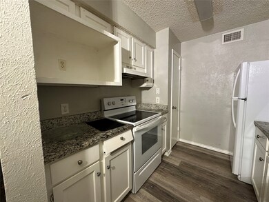 Kitchen featuring white appliances, a textured wall, a textured ceiling, white cabinetry, and dark wood finished floors