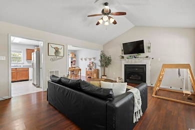 Living area with a fireplace, lofted ceiling, wood finished floors, and ceiling fan