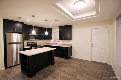 Kitchen with appliances with stainless steel finishes, dark cabinets, a kitchen island, dark wood-style flooring, and recessed lighting