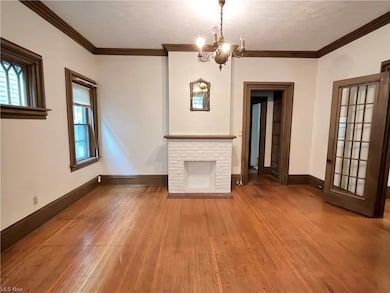 Unfurnished living room featuring an inviting chandelier, a brick fireplace, crown molding, and wood-type flooring