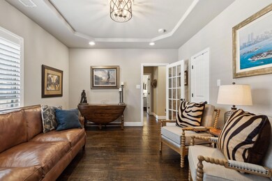 Living room with dark wood-type flooring, a raised ceiling, and an inviting chandelier