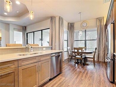 Kitchen featuring stainless steel appliances, dark wood-style flooring, decorative light fixtures, light countertops, and a tray ceiling