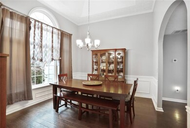 Separate Dining room featuring tall tray ceilings, new windows, arched walkways, a chandelier, wood floors, wainscoting, and crown molding