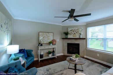 Living room with ornamental molding, a tiled fireplace, wood finished floors, and ceiling fan