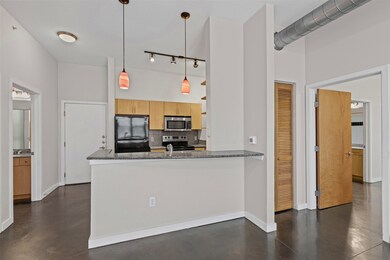 Kitchen featuring backsplash, concrete flooring, appliances with stainless steel finishes, hanging light fixtures, and a peninsula