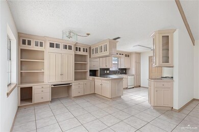 Kitchen featuring cream cabinets, white dishwasher, open shelves, a textured ceiling, and a peninsula