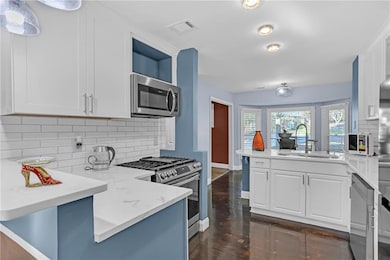 Kitchen with a peninsula, tasteful backsplash, appliances with stainless steel finishes, and white cabinetry