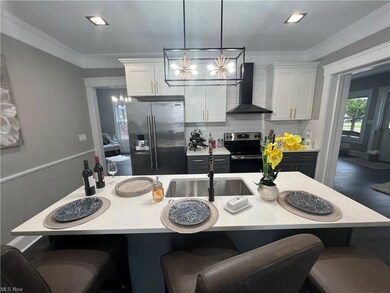 Kitchen featuring wall chimney range hood, white cabinetry, tasteful backsplash, stainless steel appliances, and decorative light fixtures