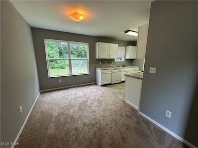 Kitchen with white cabinets, light carpet, white dishwasher, and light stone countertops