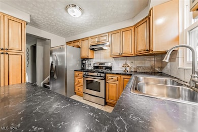 Kitchen featuring decorative backsplash, appliances with stainless steel finishes, dark stone countertops, a textured ceiling, and under cabinet range hood
