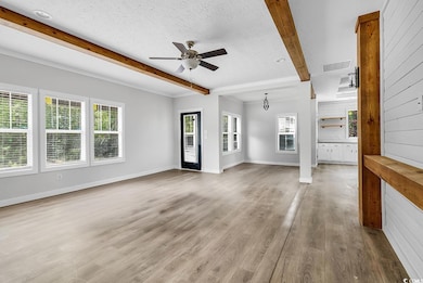 Unfurnished living room featuring beam ceiling, a ceiling fan, a textured ceiling, and light wood-style floors