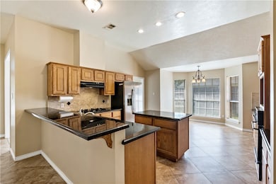 Kitchen featuring brown cabinets, a kitchen island, vaulted ceiling, tasteful backsplash, and stainless steel refrigerator with ice dispenser