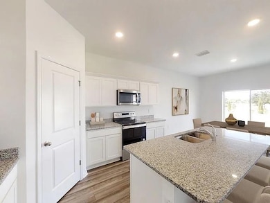Kitchen featuring stainless steel appliances, white cabinets, light stone countertops, light wood-style flooring, and a kitchen bar