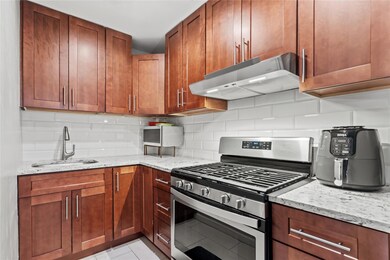 Kitchen with stainless steel range with gas cooktop, a sink, under cabinet range hood, light stone countertops, and tasteful backsplash