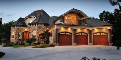 View of front of home featuring a balcony, stone siding, roof with shingles, and concrete driveway