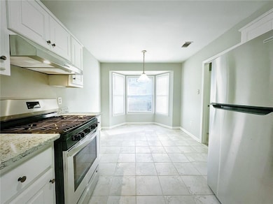 Kitchen featuring stainless steel appliances, under cabinet range hood, white cabinetry, baseboards, and hanging light fixtures