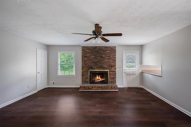 Unfurnished living room with a textured ceiling, ceiling fan, wood finished floors, and baseboards