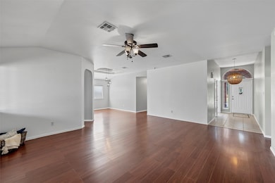 Unfurnished living room with dark wood-style floors, arched walkways, and a ceiling fan