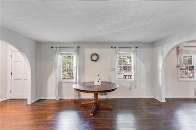 Dining area featuring arched walkways, wood-type flooring, plenty of natural light, and a textured ceiling