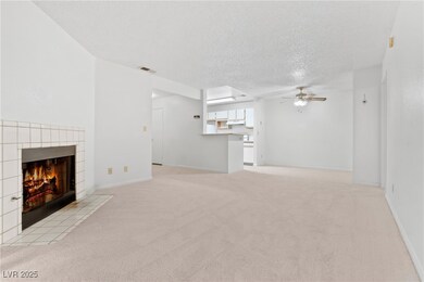 Unfurnished living room with ceiling fan, light carpet, a fireplace, and a textured ceiling