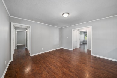 Unfurnished room with attic access, ornamental molding, a textured ceiling, and dark wood finished floors