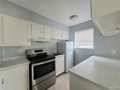 Kitchen with stainless steel range with electric cooktop, under cabinet range hood, freestanding refrigerator, white cabinets, and a textured ceiling