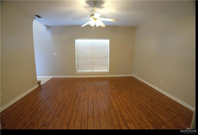 Empty room featuring arched walkways, wood finished floors, and a ceiling fan