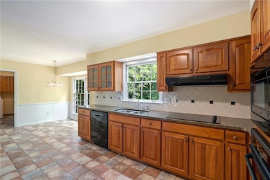 Kitchen featuring black appliances, under cabinet range hood, a sink, brown cabinets, and a chandelier