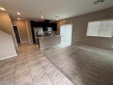 Kitchen featuring dark cabinetry, open floor plan, light tile patterned floors, light stone countertops, and a kitchen island with sink
