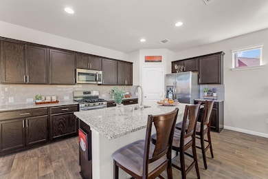 Kitchen with decorative backsplash, dark brown cabinetry, a breakfast bar area, light stone countertops, and light wood-style floors