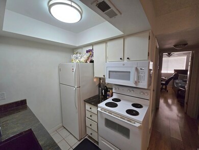 Kitchen featuring white appliances, dark countertops, white cabinetry, a tray ceiling, and a ceiling fan