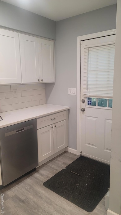 Kitchen with white cabinets, dishwashing machine, light wood-type flooring, and decorative backsplash